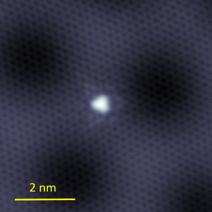 scanning tunneling micrograph showing graphene with a single atomic defect as a white dot in the center.
