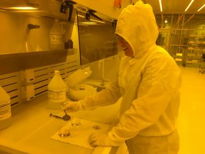 a woman in a cleansuit works with qubit components in a yellow-hued research cleanroom