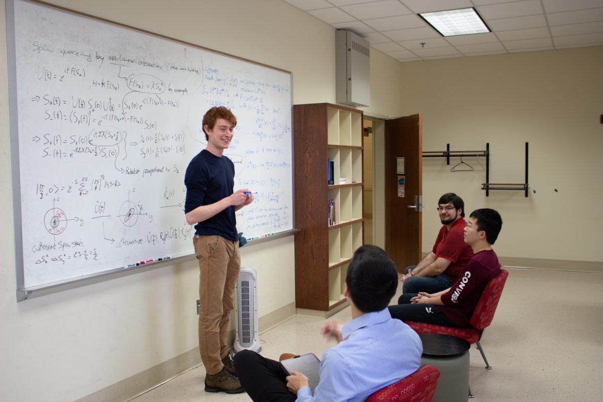 a group of students in front of a white board with physics equations on it