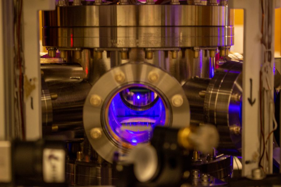 a metal device with a circular hole in the center has a glowing small orb of blue superchilled strontium atoms glowing inside the metal chamber