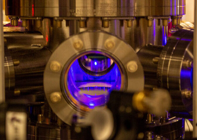 a metal device with a circular hole in the center has a glowing small orb of blue superchilled strontium atoms glowing inside the metal chamber